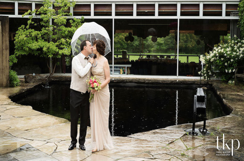 Bridge and groom kiss under an umbrella in front of the Arboretum Centre's reflecting pool