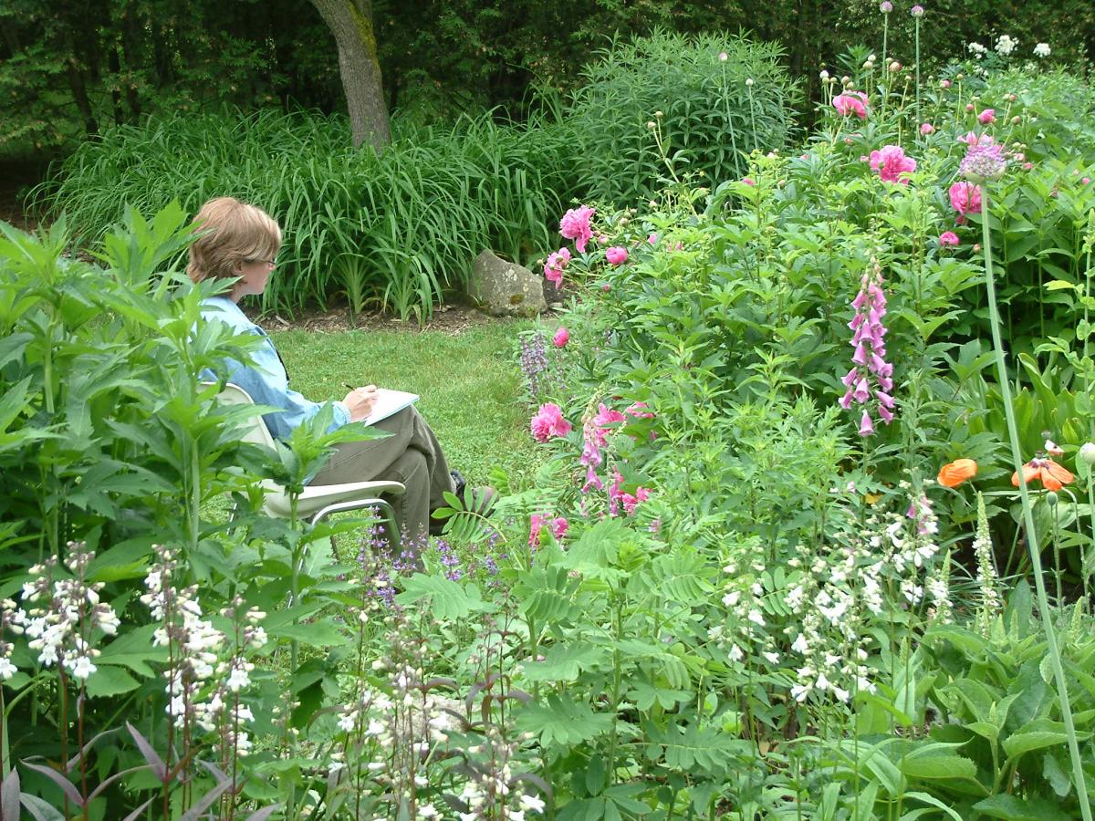 Woman sits on bench and sketches flowers in garden