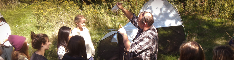 workshop instructor points to a small specimen in a jar in the field