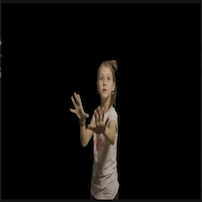 A young girl standing in a dark backdrop. She expresses a sense of wonder through her facial expression and body language