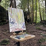 easel with painting, painting tray set up in woods